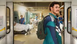 A student standing inside a train carriage, with a hospital room just outside the doors.