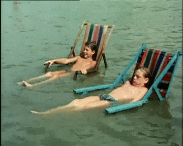 Two young boys sit on deck chairs that are submerged in water