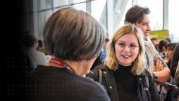 A young woman with glasses smiles while conversing with a Swinburne staff member at a crowded study expo event.