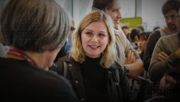 A young woman with glasses smiles while conversing with a Swinburne staff member at a crowded study expo event.