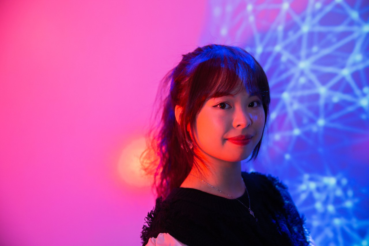 A female student lit by red light and a blue projection of a complex network.