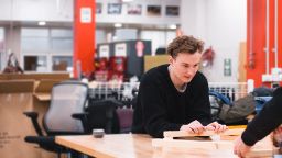 Student sits at table in classroom with hands on some pieces of wood.