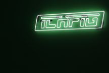 A florescent green sign of the ICHPIG® logo against a dark wall