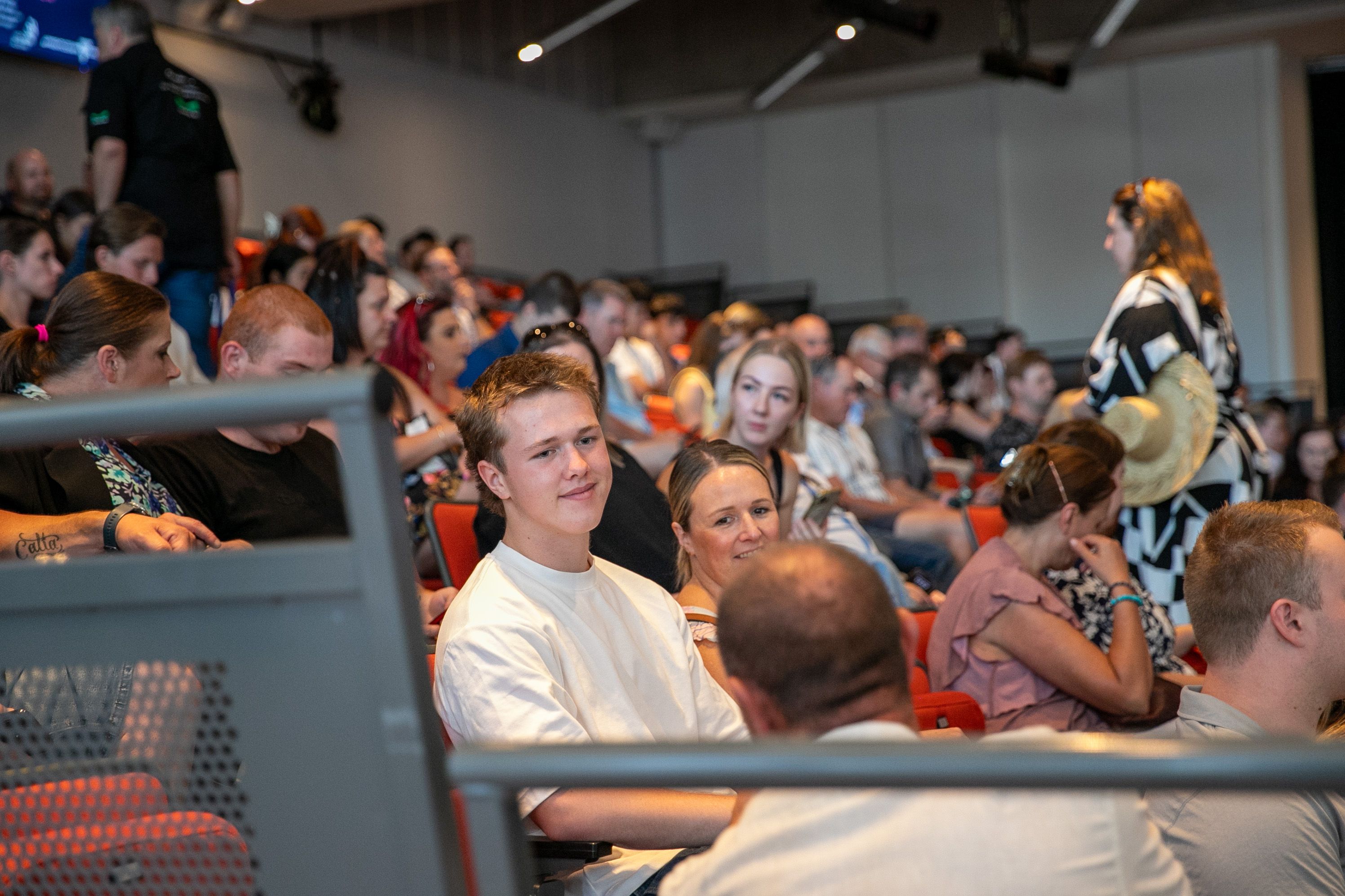 WorldSkills Regional Awards 2025 -2 Man is sitting in an crowded auditorium smiling and looking at a person sitting in front of them, having a conversation.