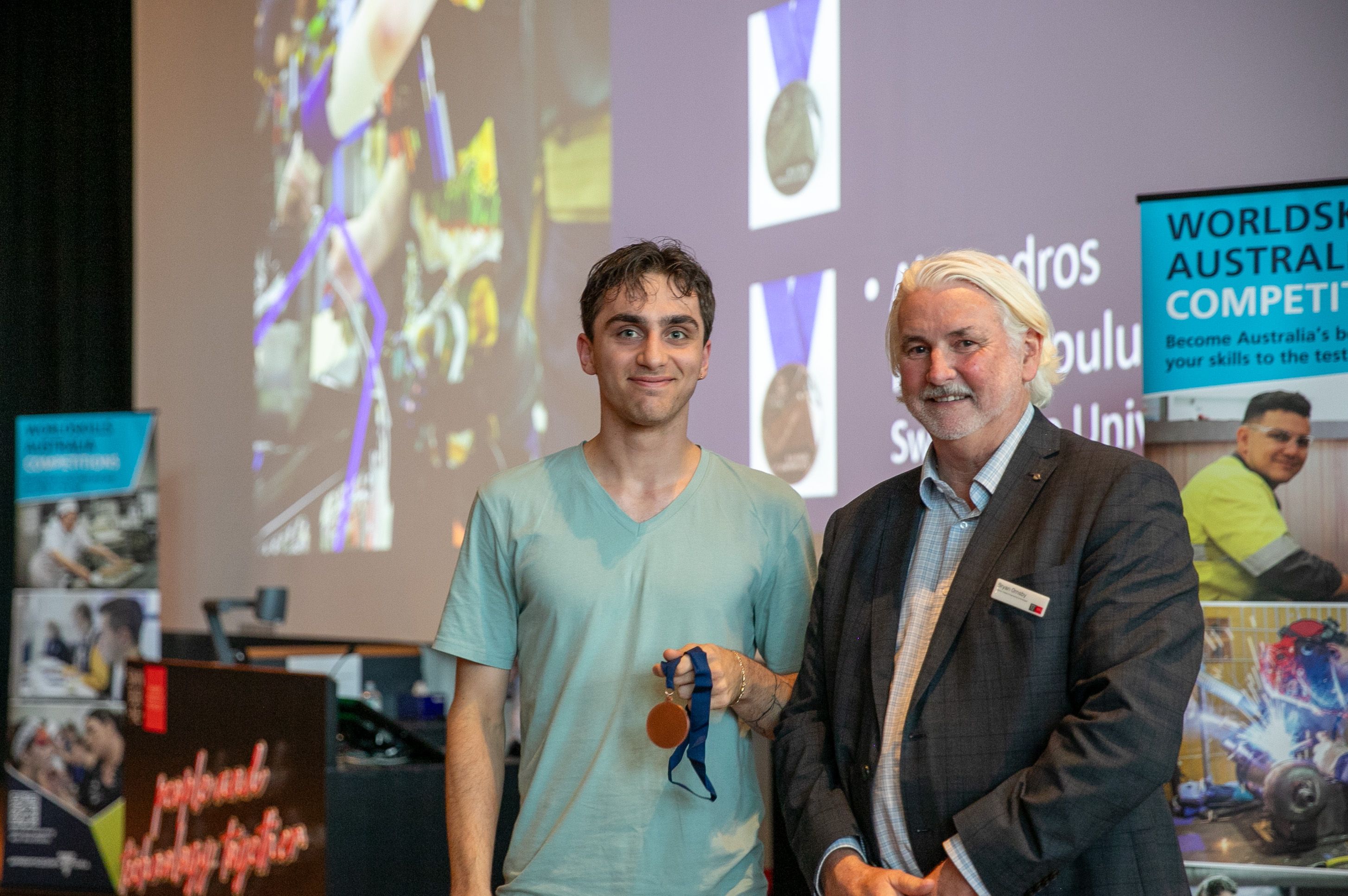 WorldSkills Regional Awards 2025 -3 Male student standing next to teacher, holding a bronze medal and smiling.