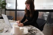 A student types on her computer in an office. Next to her computer on the table is a 3D printed model of a building.