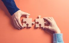 Two hands connecting puzzle pieces against an orange background