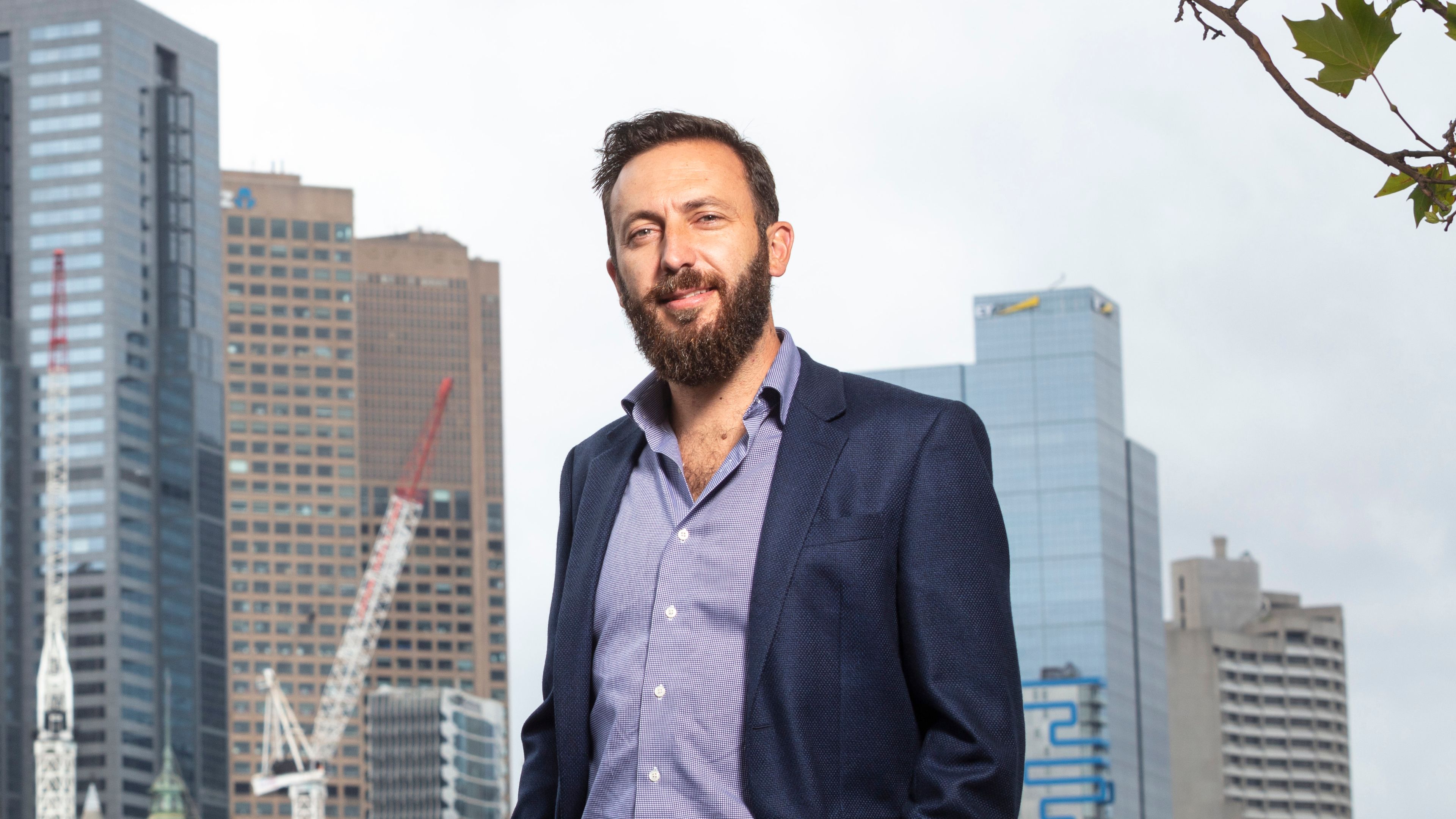 Mid-shot of Peter Nguyen wearing a blue suit jacket and smiling to camera with the Melbourne CBD in the background