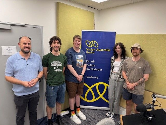 Vision Australia Radio with Swinburne students and Peter Marcato Five people smiling and standing in front of a blue and yellow Vision Australia Radio banner.