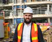 Photograph of Peter Moran standing in front of a construction site wearing a safety vest and hard hat.