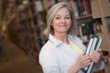 Mature age woman holding books in a library.