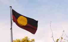 The Aboriginal flag flying high in the wind outdoors. 