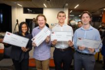 Four people facing the camera smiling, holding up printed out cheques.