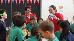 A group of primary school children in a classroom with two PrimeSCI! educators. One educator is holding a squeezy ball of the planet Earth. One child is holding a slinky toy. 