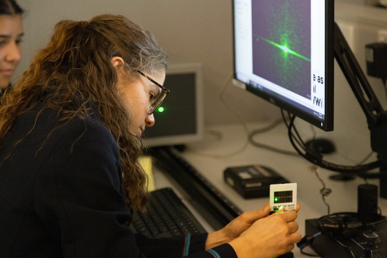 Young girl fixing a device in her hands while sitting in a classroom.