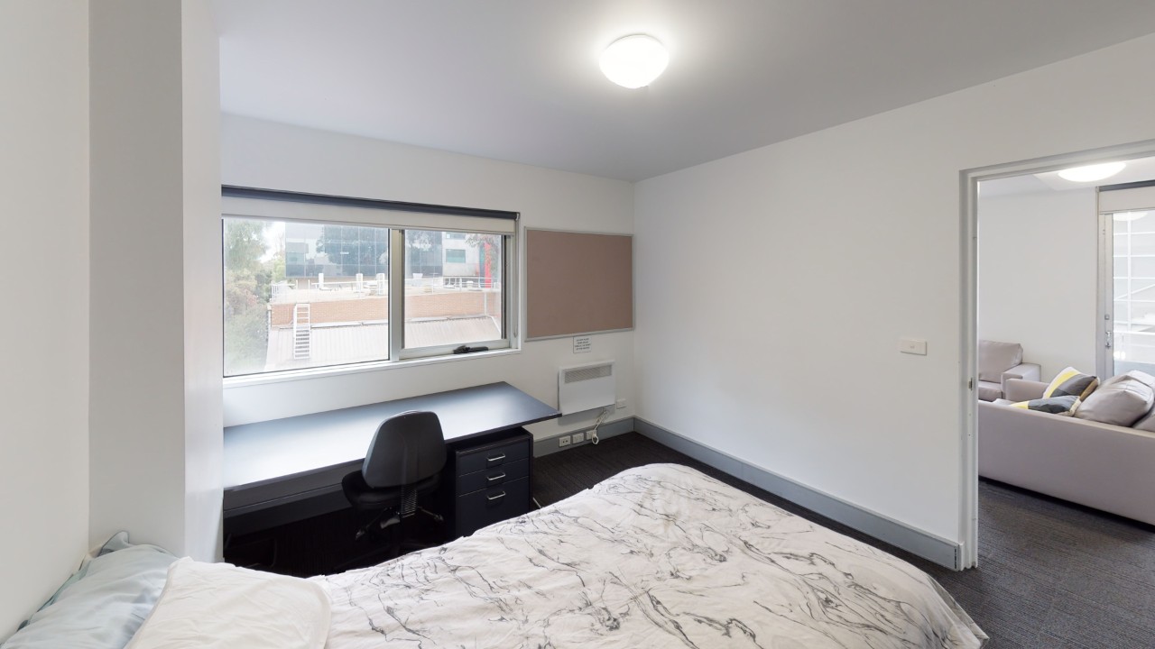 Room of an apartment showing half a bed, desk and chair