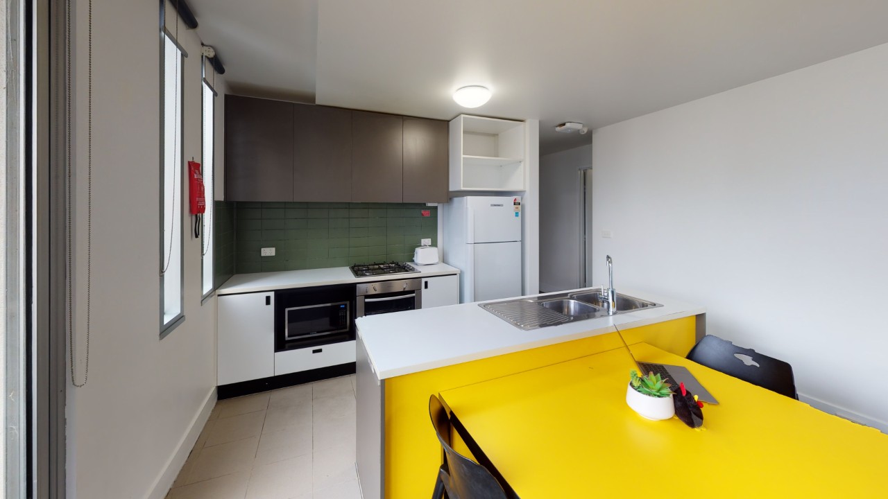 A kitchen including a fridge, island bench and bright yellow dining table