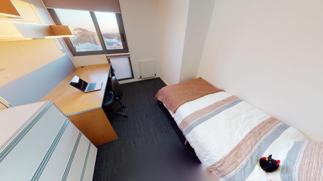 A bedroom with a bed and stripy doona cover, desk, laptop, chair and shelving