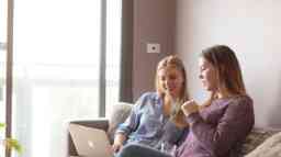 Two female students relax on a couch with a laptop open