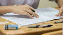 Student using a pencil, reading information on white exam paper.