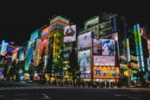 An image of a city in Japan at night time, with billboards lit up and crowds of people shopping.