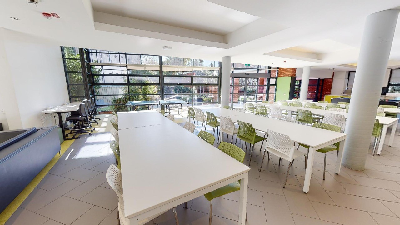 A large room with white long tables and green and white chairs