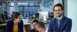 Male graphic designer smiling while colleague interacting over blueprint in background.