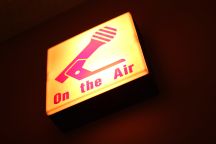 A yellow sign with a picture of a microphone and the words 'on the air' in red. 