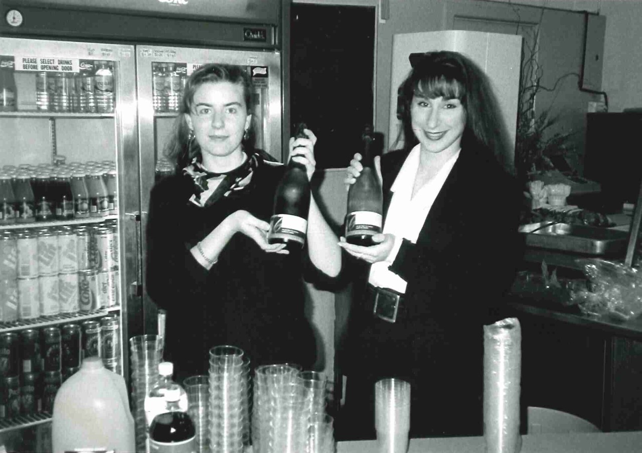 Two women hold champagne bottles in a bar