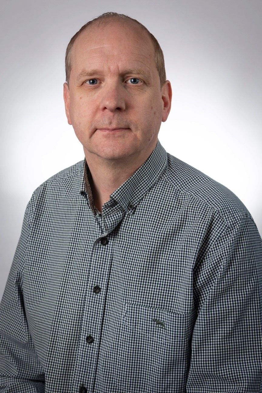 Headshot of Andrew Carroll wearing a green chequered shirt