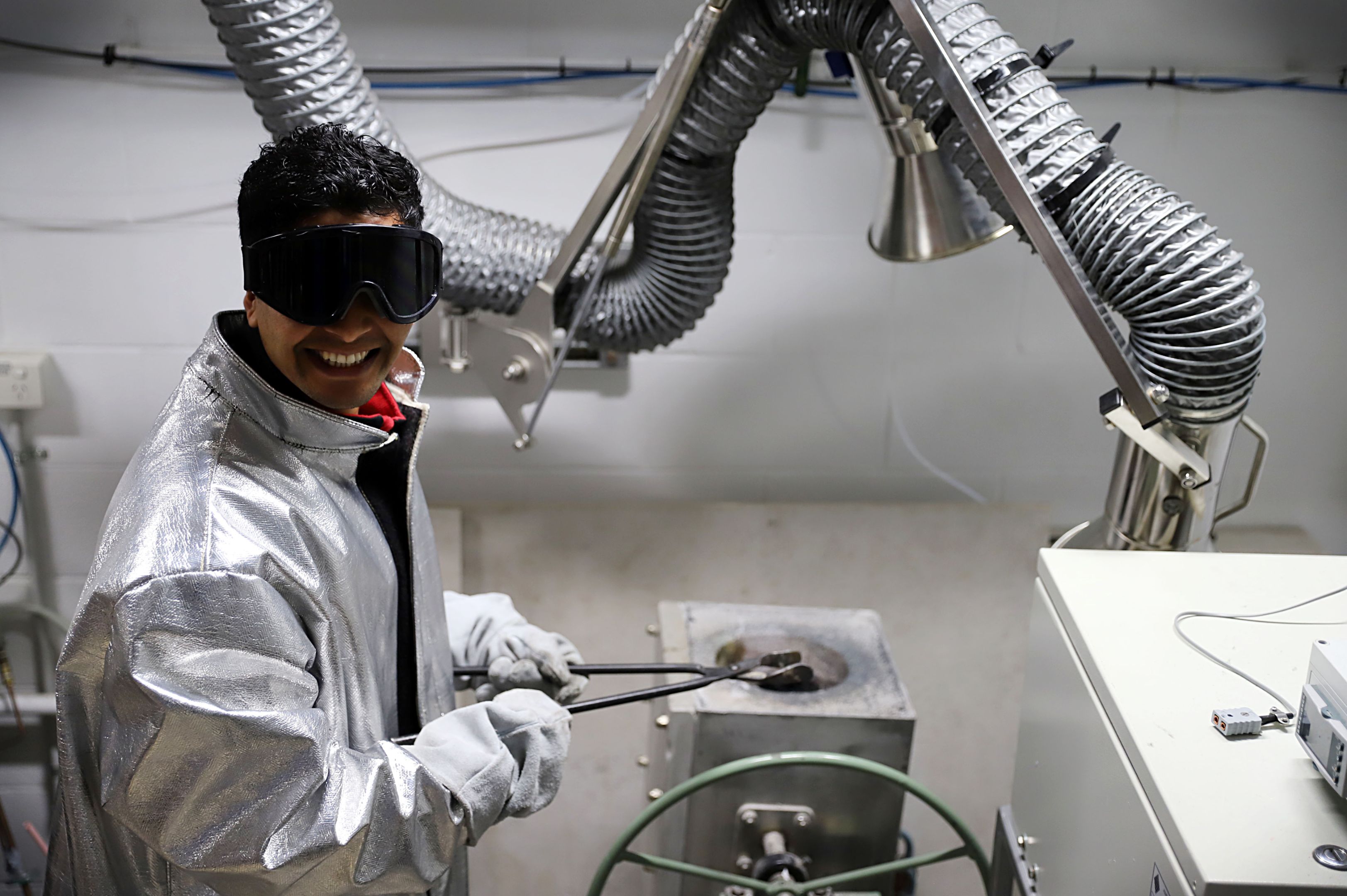 A man in a silver protective jacket and black protective eye goggles folds metal forceps in a scientific research lab