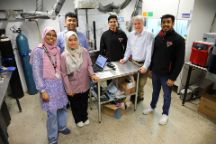 Six researchers stand in a scientific research lab with high tech machinery and equipment