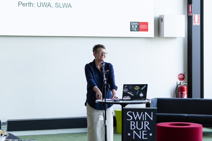 Professor Melanie Swalwell stands at a lectern speaking at the launch event of her new project, The Australian Emulation Network.