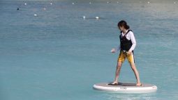 A woman standing on a Wheebo on a calm body of water