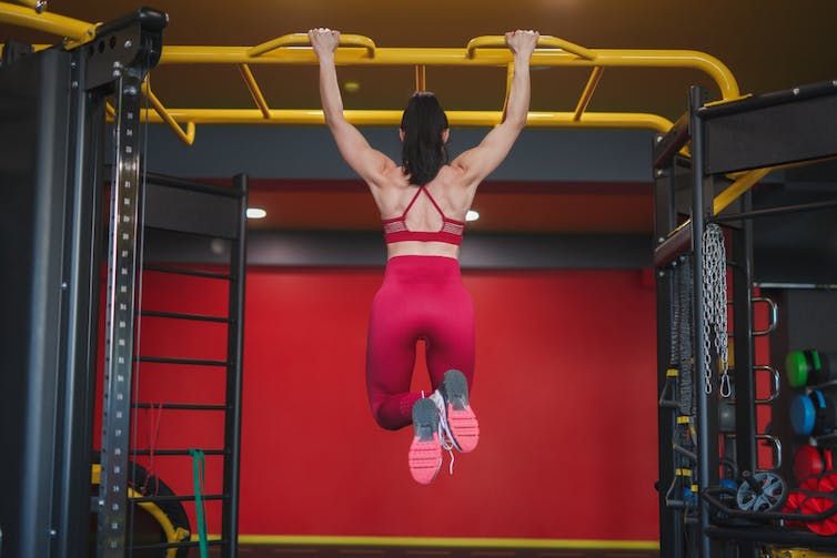 How to do a dead hang safely Women with her back turned performing a dead hang in the gym