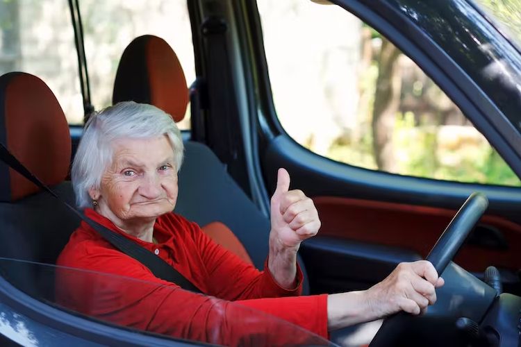 Elderly woman driving Elderly woman driving a car, looking at the camera smiling and holding her left up, giving the thumbs up