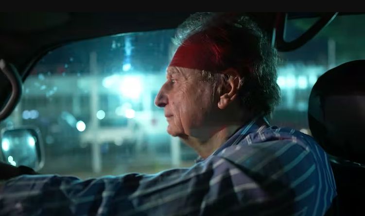 Elderly man driving at night Side profile of an elderly man driving a car at night, with white hair and a blue striped shirt