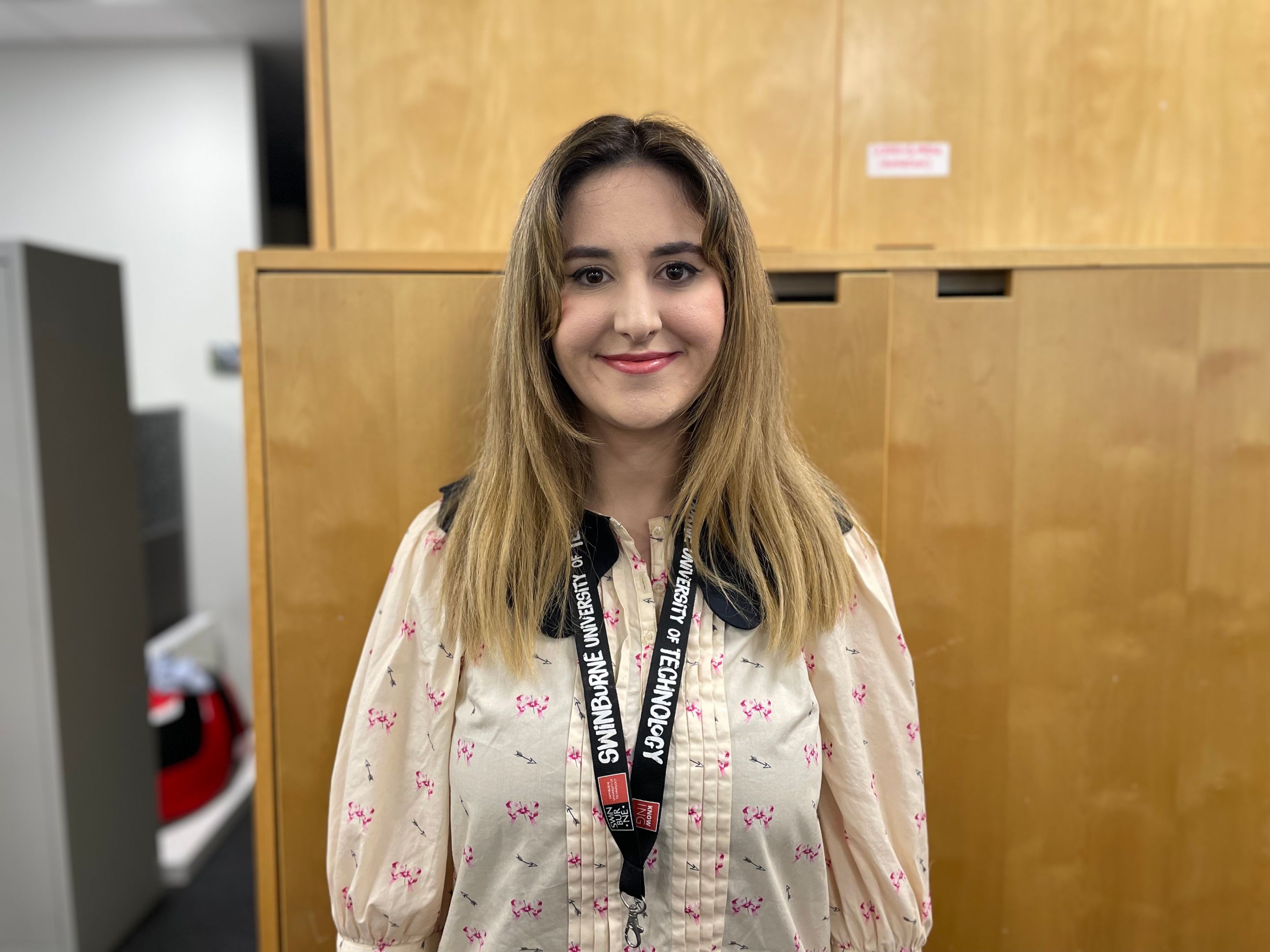 Woman standing face to camera smiling wearing a blouse and lanyard