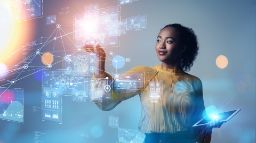 Young girl holding a tablet and with her other hand reaching out to touch a floating holographic diagram. 