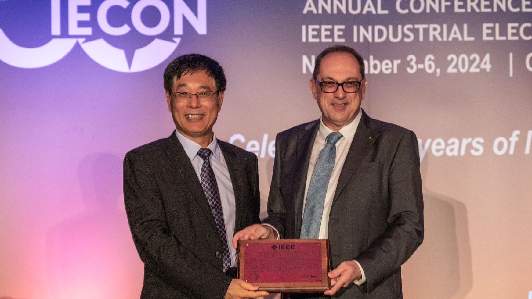 Swinburne’s Distinguished Professor Qing-Long Han (left) stands next to a second man on stage accepting the Dr -Ing. Eugine Mittelmann Achievement Award. They are both holding the award and smiling at the camera