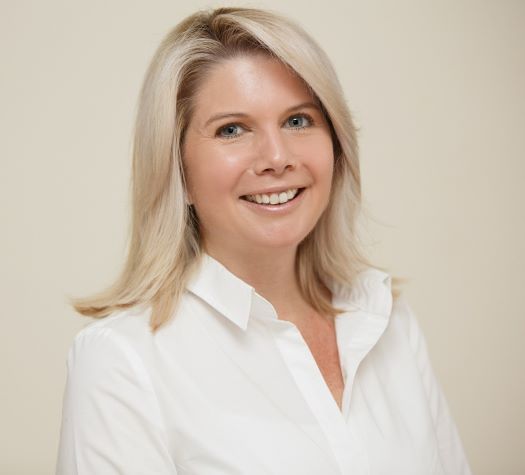 Woman with blond hair wearing a white blouse smiling at the camera