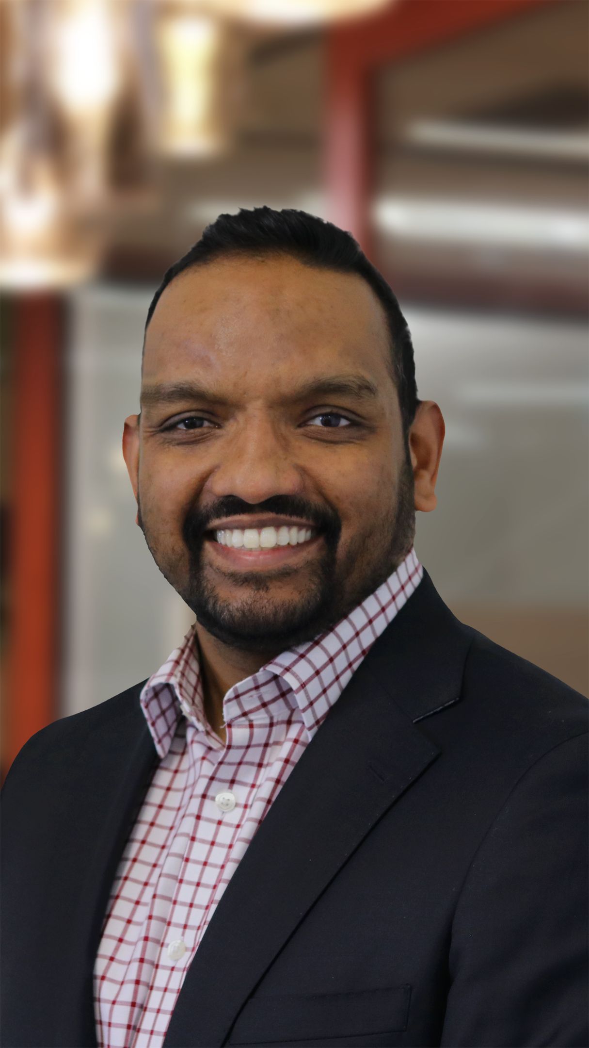 Man in a checkered  shirt and black blazer smiling for the camera