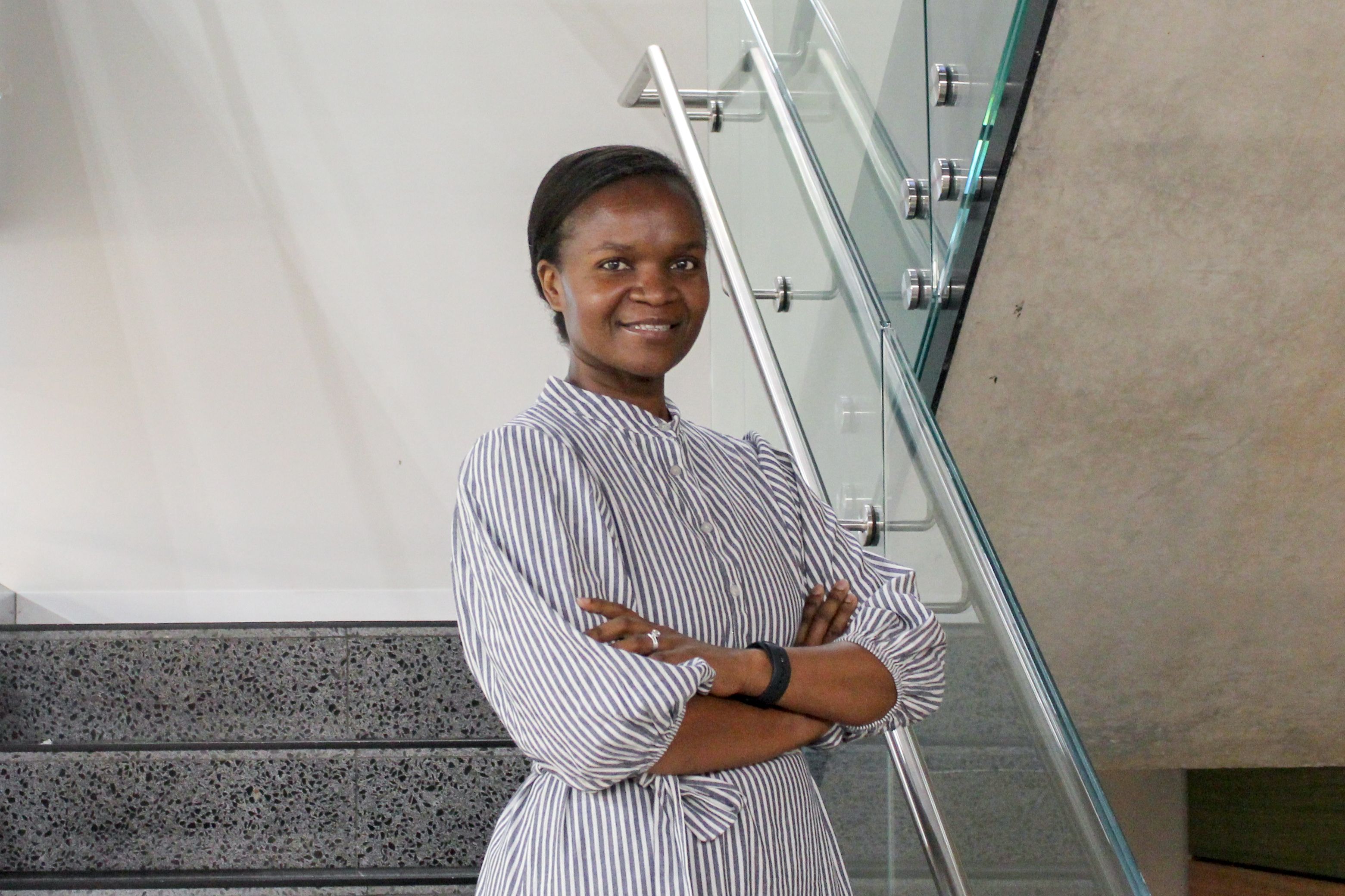 Swinburne Staff Member Antoinette Gwasira standing on a set of concrete stairs with a glass railing and a white wall behind. 