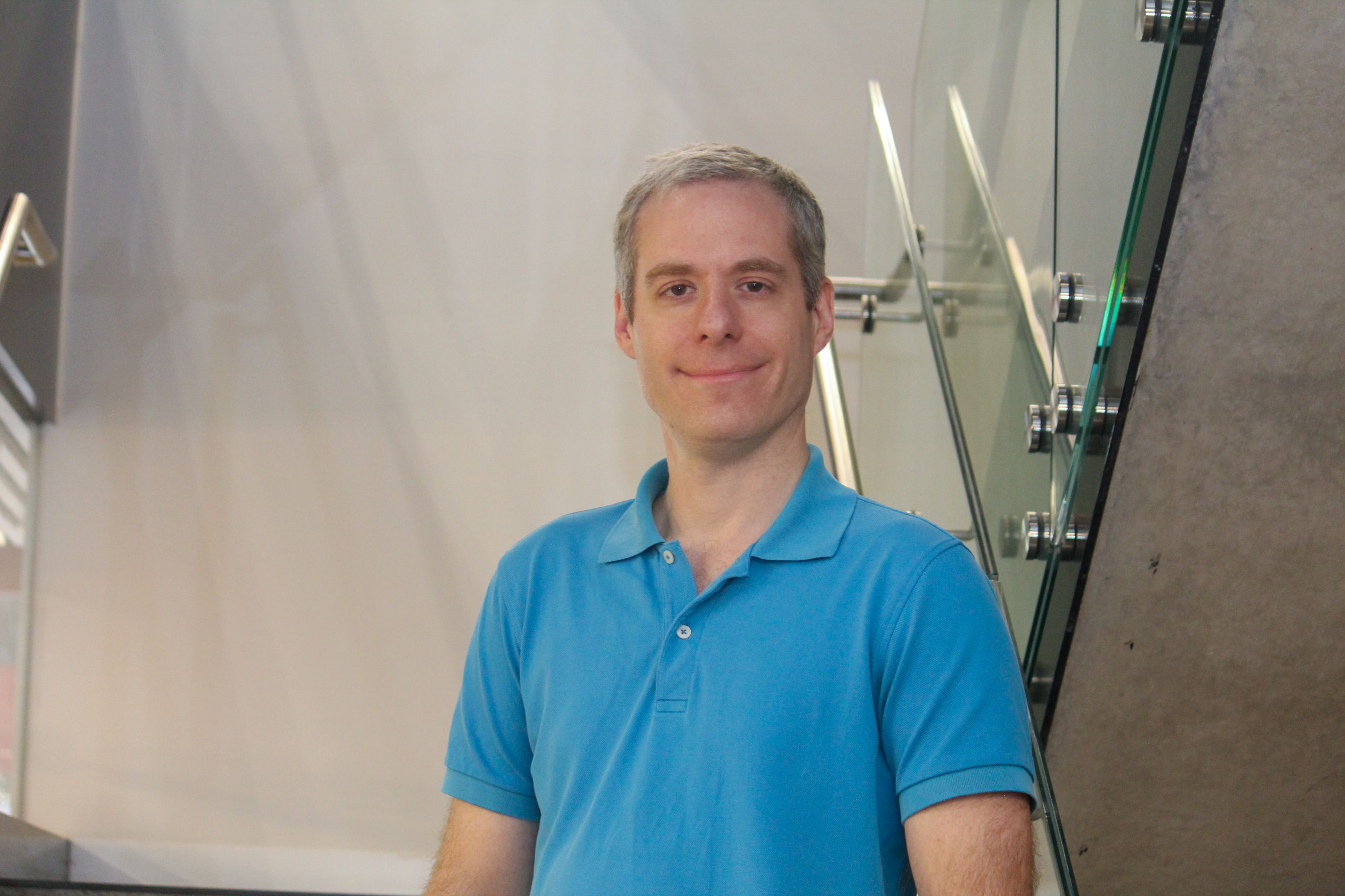 Swinburne Staff Member Ant Sowards standing on a set of concrete stairs with a glass railing and a white wall behind. 