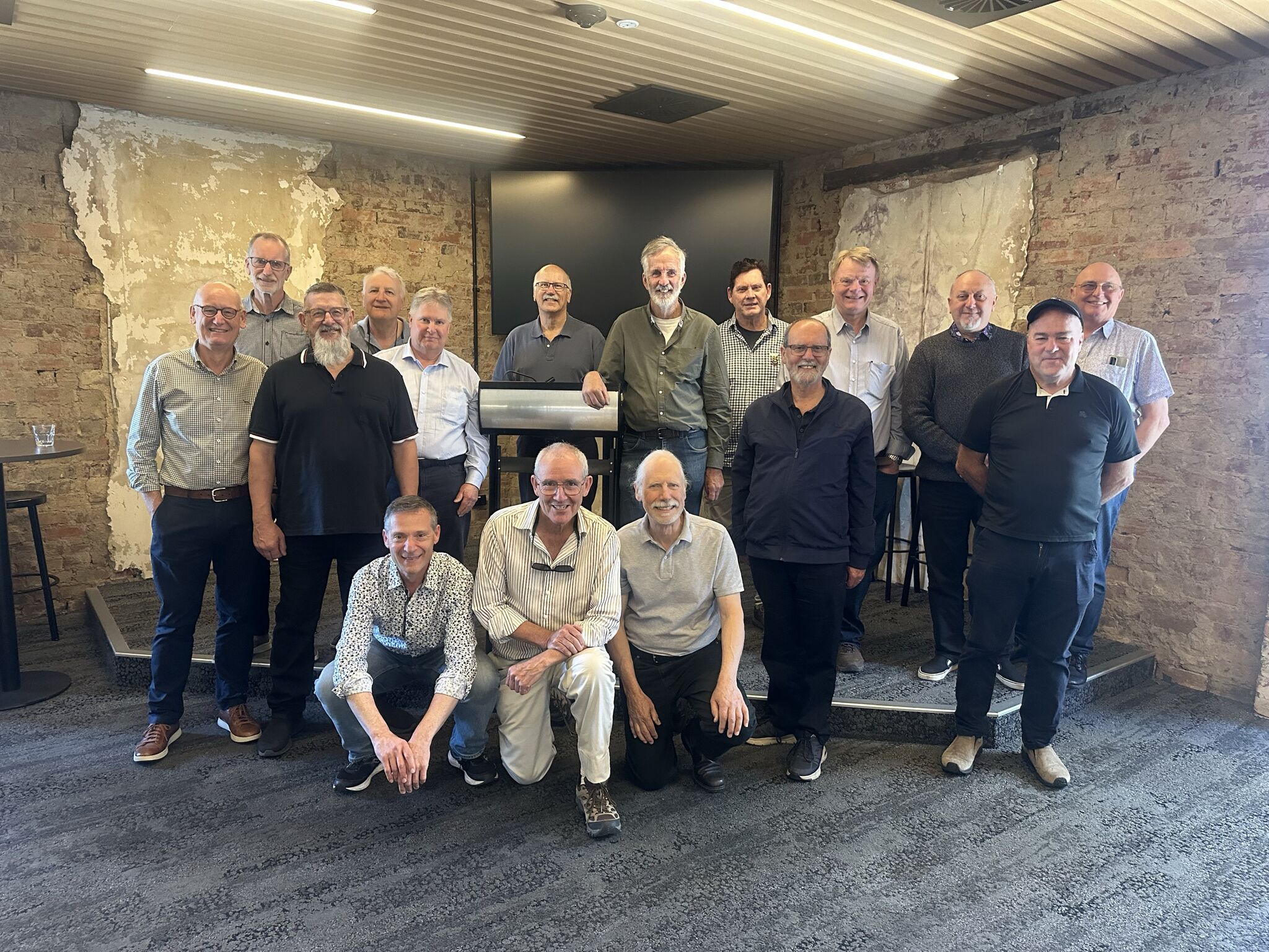 Group of elderly people pose in front of a podium. Some are standing and some are crouching down