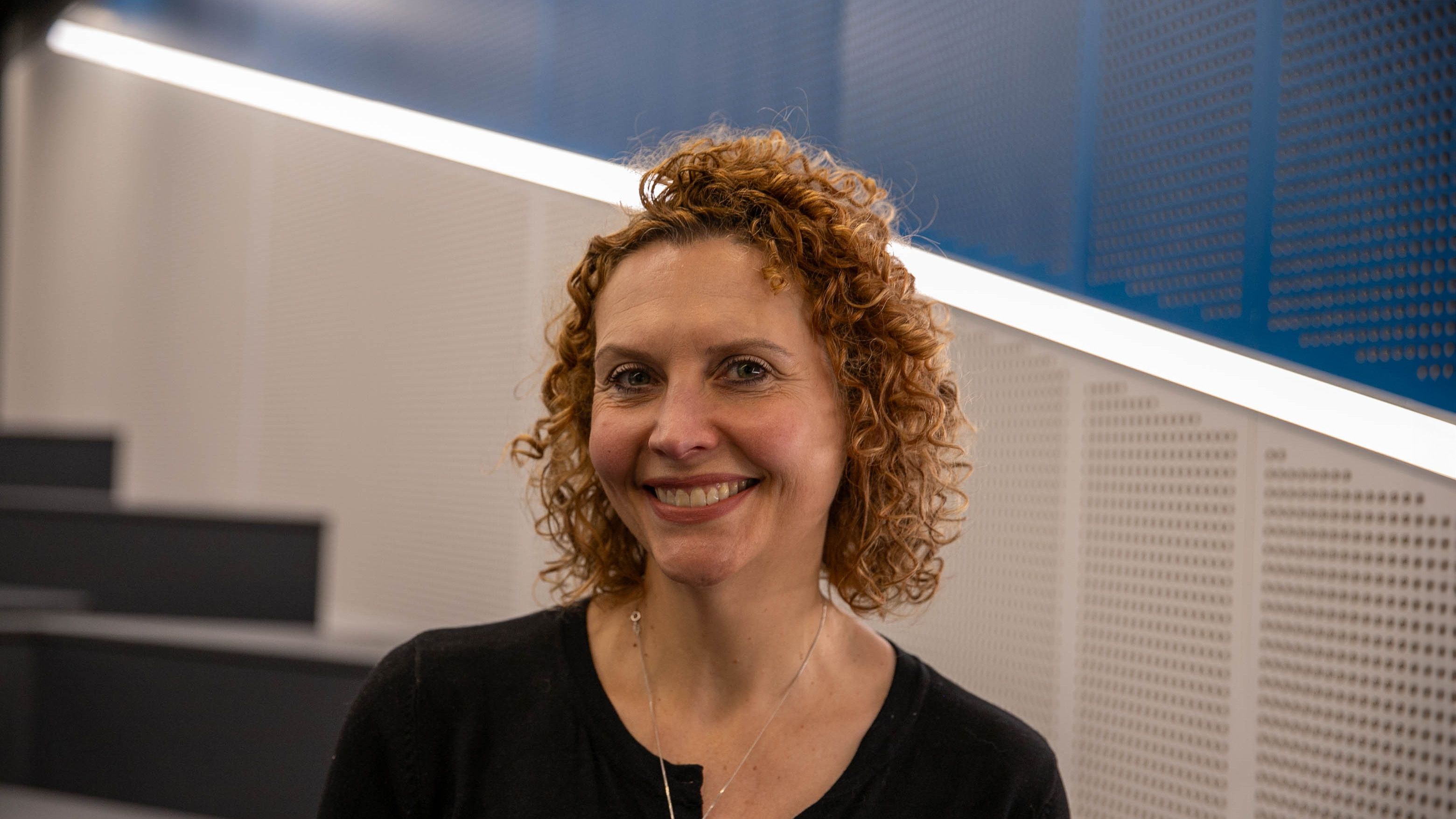 Woman in a black top, with curly hair, smiling for the camera.