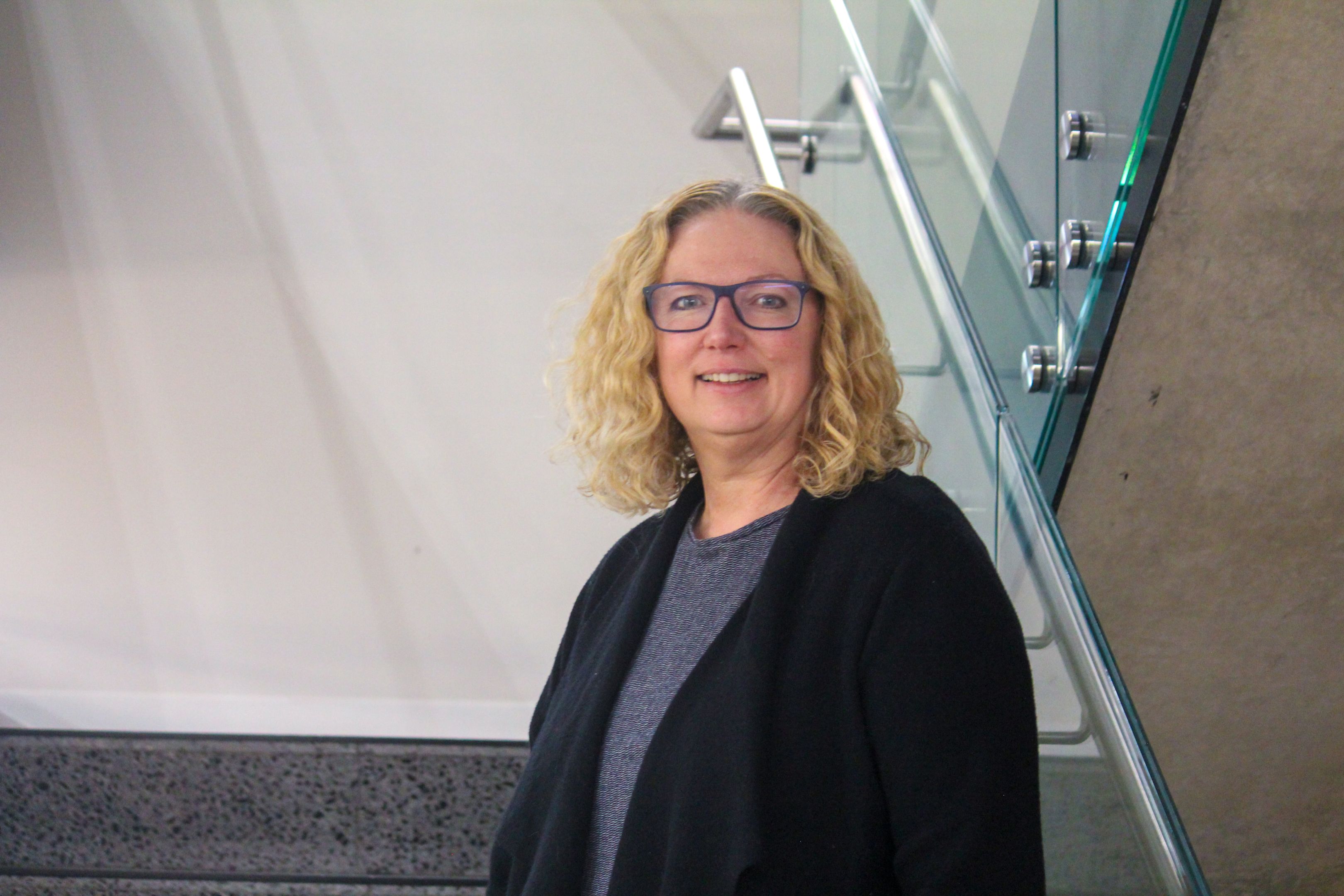 Swinburne Staff Member Nicola Howard standing on a set of concrete stairs with a glass railing and a white wall behind. 