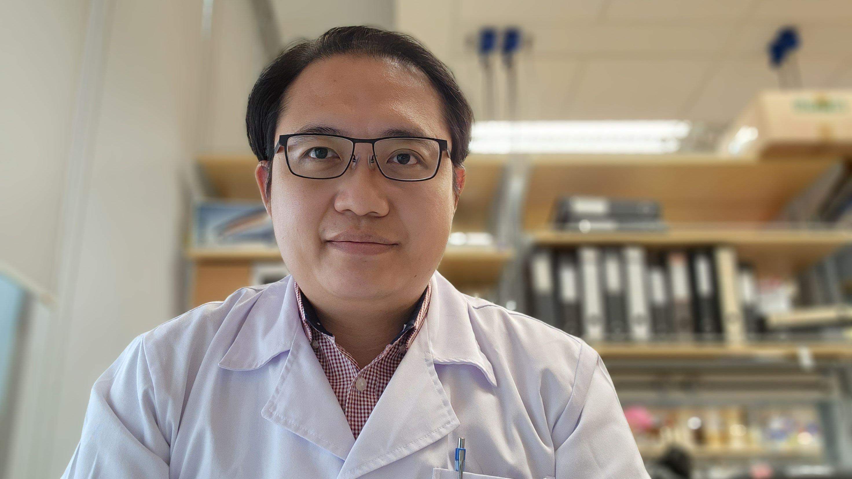 Man facing front on and smiling at the camera, wearing glasses and a science coat