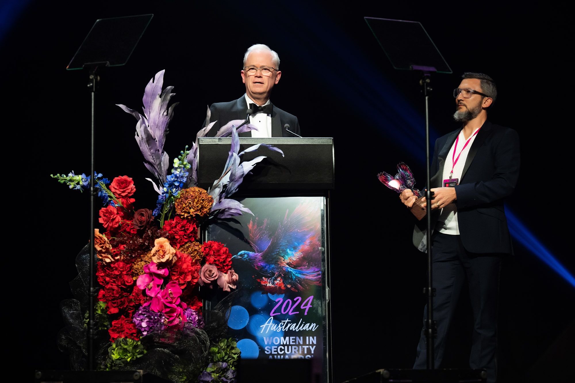 Rhys Shobbrook accepting an award on a podium with colourful flowers in front