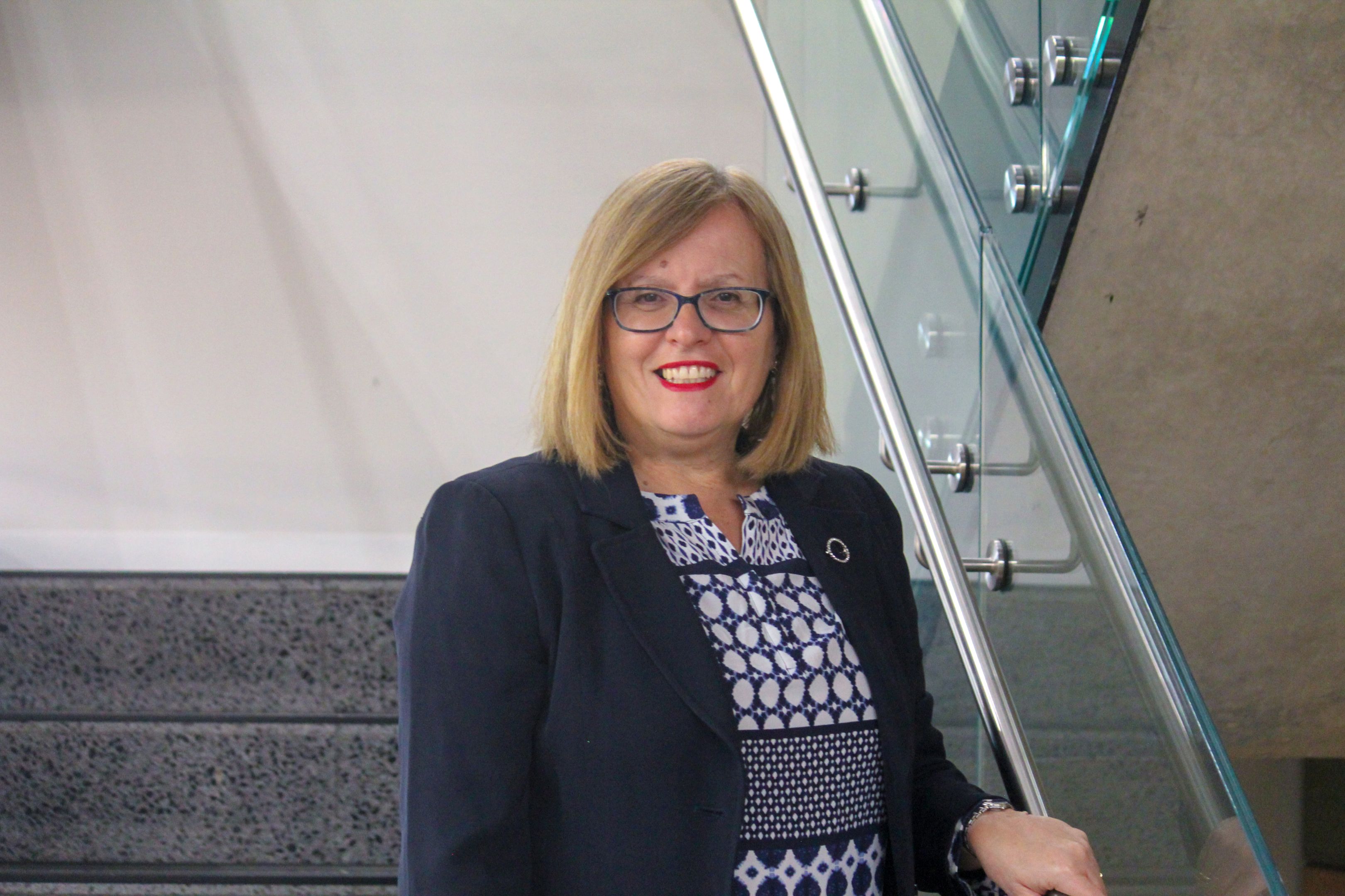 Swinburne Staff Member Sandra Woods standing on a set of concrete stairs with a glass railing and a white wall behind. 